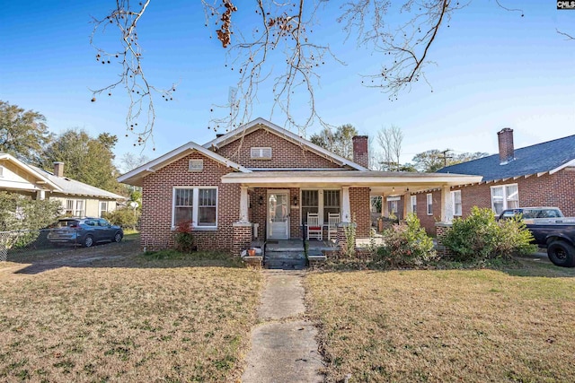 view of front of home with covered porch, brick siding, a chimney, and a front lawn