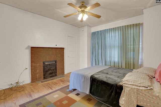 bedroom with a fireplace, a ceiling fan, and wood finished floors