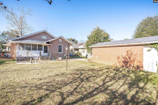 rear view of property featuring a sunroom, a lawn, and brick siding