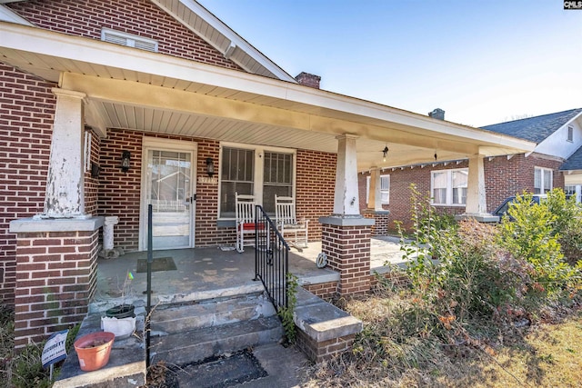 view of front of house with a chimney, a porch, and brick siding