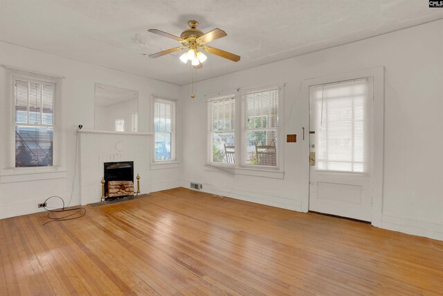 unfurnished living room with a ceiling fan, visible vents, a fireplace, and light wood-style flooring