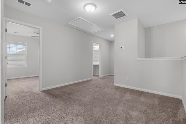 carpeted empty room with attic access, visible vents, and baseboards