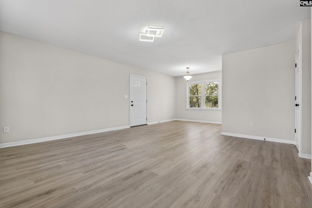 spare room with light wood-style floors, visible vents, baseboards, and a textured ceiling