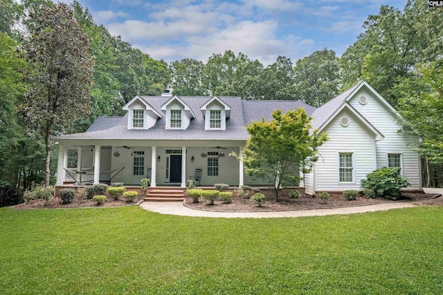 new england style home with ceiling fan, a front lawn, roof with shingles, and a porch