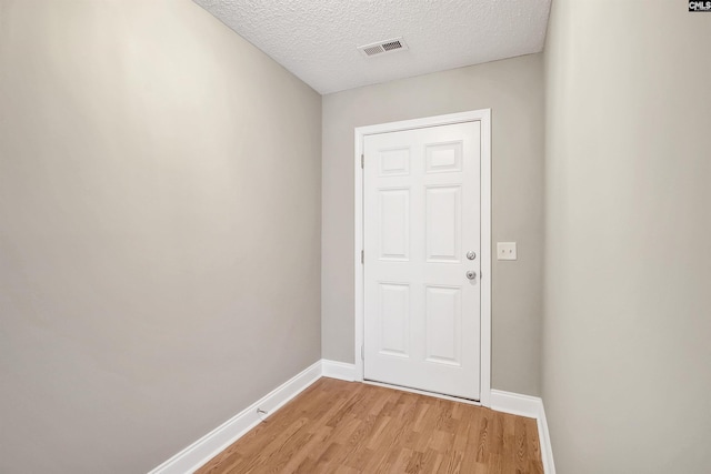 entryway with baseboards, visible vents, a textured ceiling, and light wood finished floors