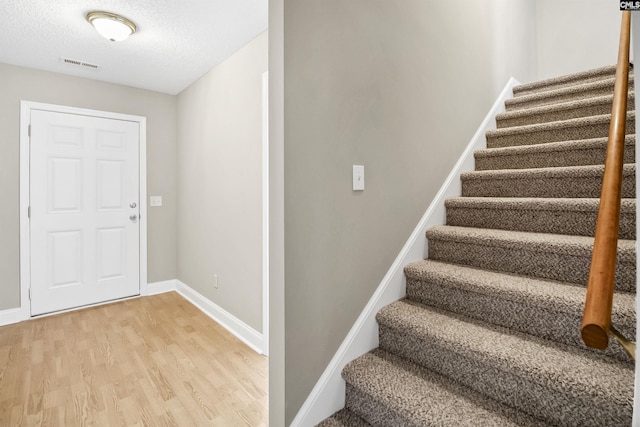 stairs featuring a textured ceiling, wood finished floors, visible vents, and baseboards