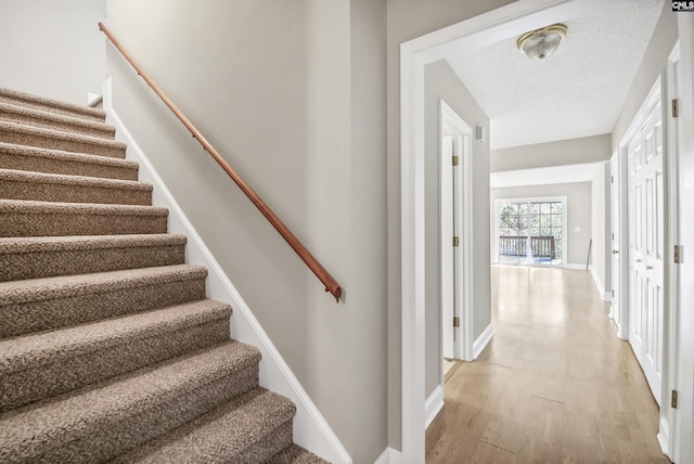 stairs with a textured ceiling, baseboards, and wood finished floors