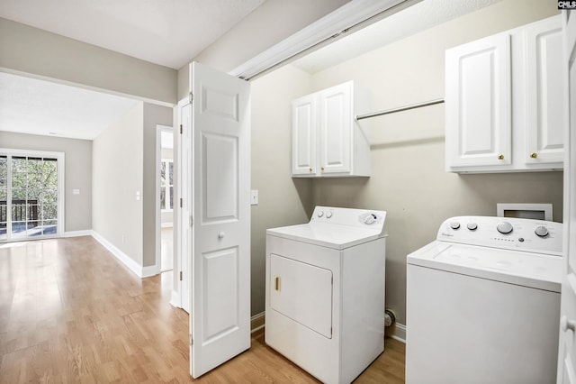 clothes washing area featuring baseboards, washing machine and dryer, cabinet space, and light wood-style floors