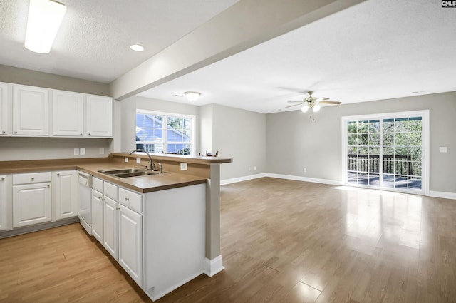 kitchen with white dishwasher, light wood-style flooring, a peninsula, a sink, and white cabinetry