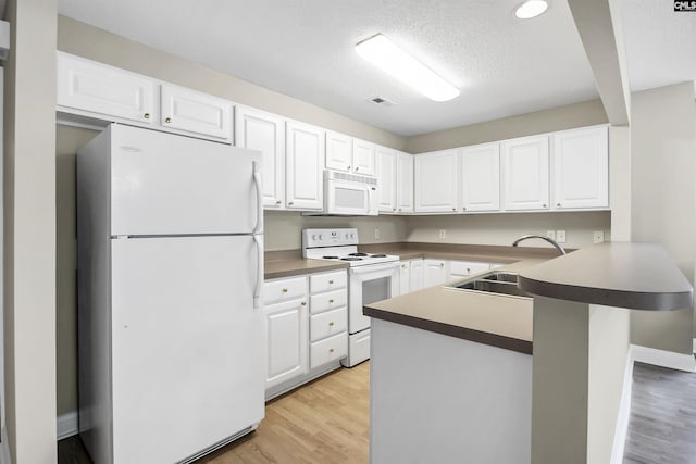 kitchen featuring white cabinets, a sink, light wood-type flooring, white appliances, and a peninsula