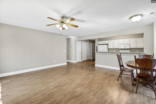 dining area with a ceiling fan, light wood finished floors, baseboards, and a textured ceiling