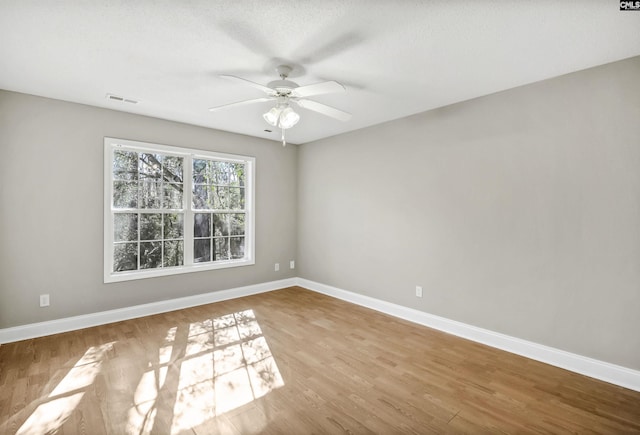 empty room with baseboards, visible vents, ceiling fan, and wood finished floors