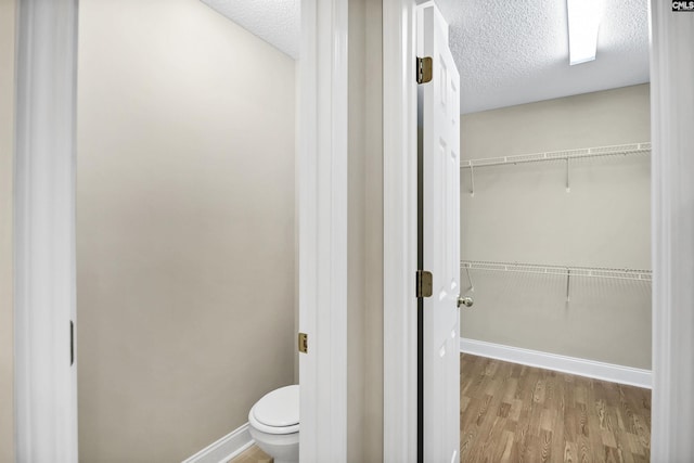 bathroom with a textured ceiling, toilet, wood finished floors, baseboards, and a walk in closet