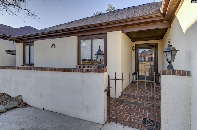 property entrance with stucco siding and roof with shingles