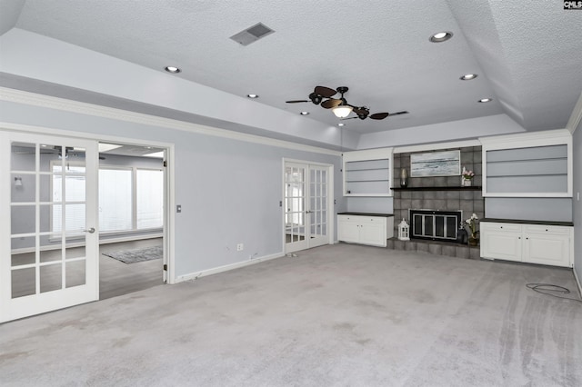 unfurnished living room featuring visible vents, a tile fireplace, light colored carpet, a tray ceiling, and french doors