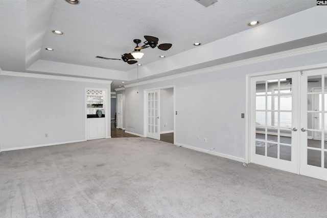 empty room with carpet, a raised ceiling, a textured ceiling, and french doors