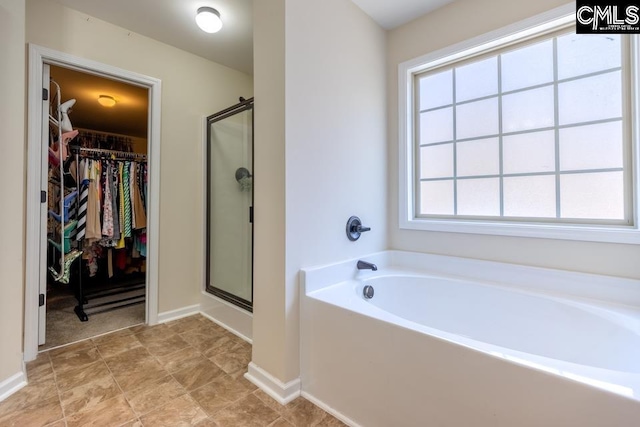 bathroom with a bath, a shower stall, a walk in closet, and baseboards