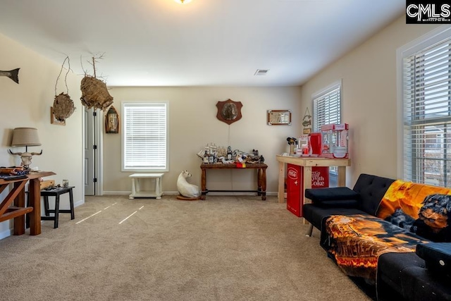 carpeted living area featuring visible vents, a wealth of natural light, and baseboards