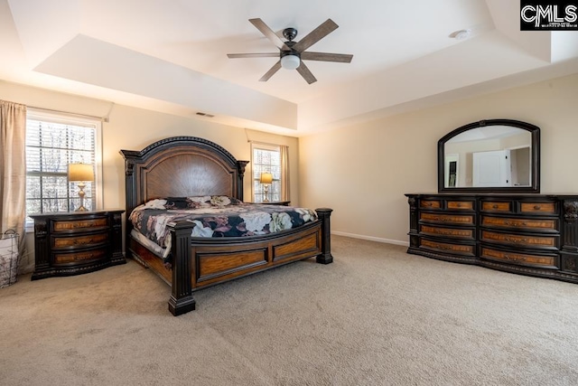 carpeted bedroom with a ceiling fan, visible vents, a tray ceiling, and baseboards