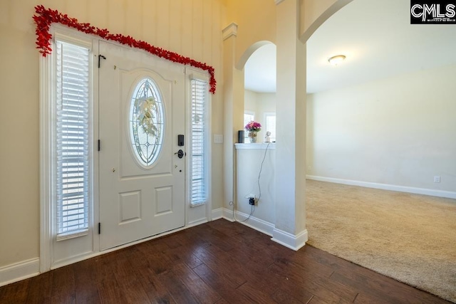 foyer with dark wood-style floors, baseboards, and arched walkways