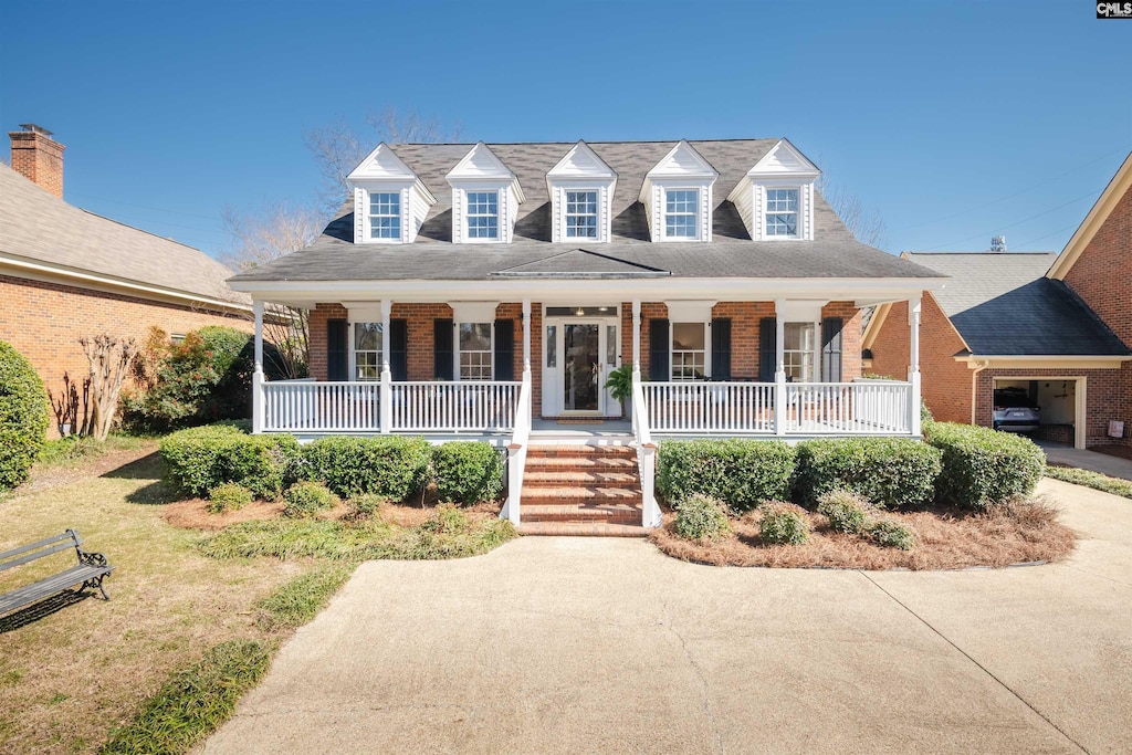 cape cod house with driveway, a porch, and brick siding