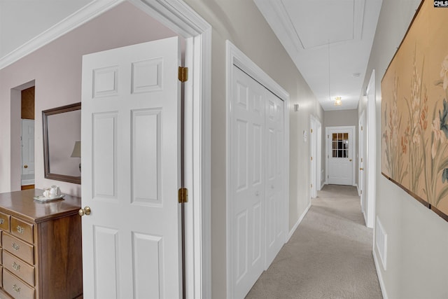 corridor with baseboards, attic access, and light colored carpet