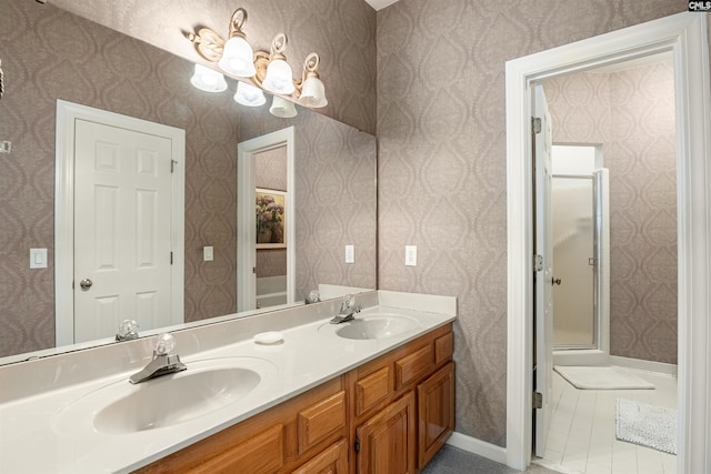 bathroom featuring double vanity, wallpapered walls, a shower with door, and a sink