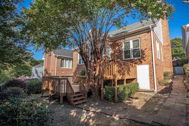 back of house featuring brick siding, a chimney, and a wooden deck