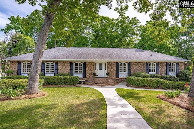 ranch-style home with brick siding, roof with shingles, and a front yard