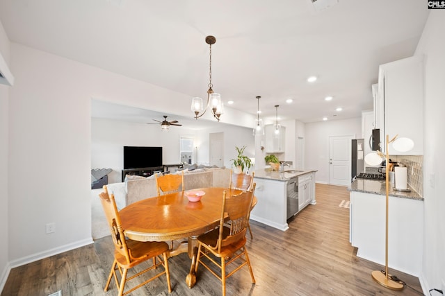 dining room with light wood-style floors, ceiling fan with notable chandelier, baseboards, and recessed lighting