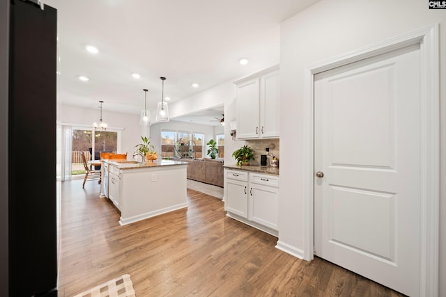 kitchen with decorative light fixtures, backsplash, open floor plan, white cabinetry, and light wood-type flooring