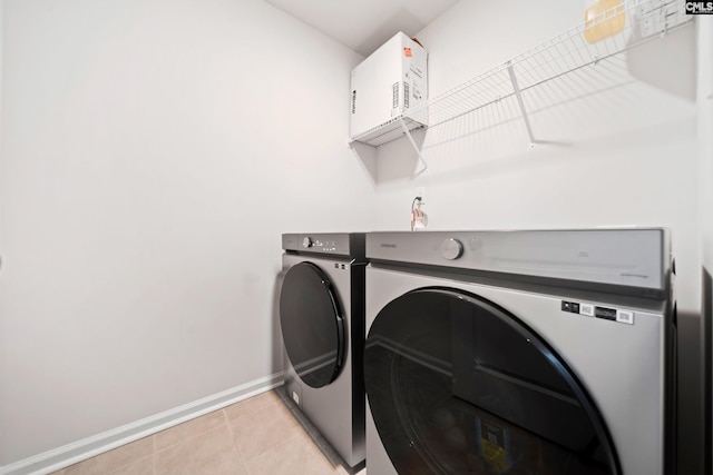 washroom featuring washing machine and dryer, laundry area, baseboards, and light tile patterned floors