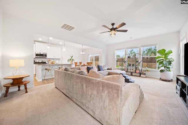 living room with recessed lighting, light colored carpet, visible vents, baseboards, and ceiling fan with notable chandelier