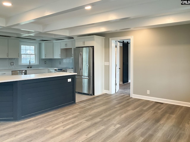 kitchen with light countertops, appliances with stainless steel finishes, light wood-style flooring, and tasteful backsplash