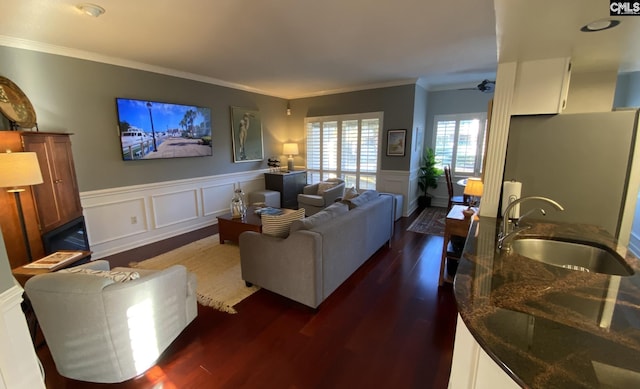 living room with a decorative wall, a wainscoted wall, dark wood-style flooring, a ceiling fan, and crown molding