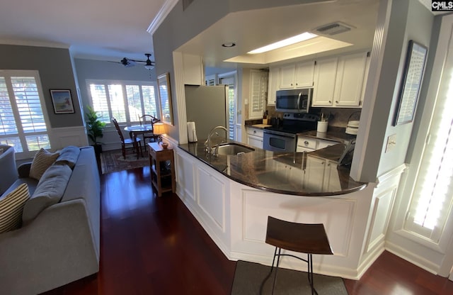 kitchen featuring stainless steel appliances, a peninsula, a sink, wainscoting, and dark countertops