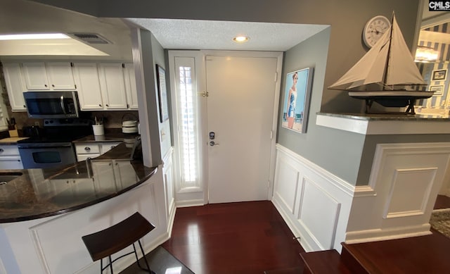 interior space featuring a textured ceiling, a decorative wall, a wainscoted wall, dark wood-type flooring, and visible vents