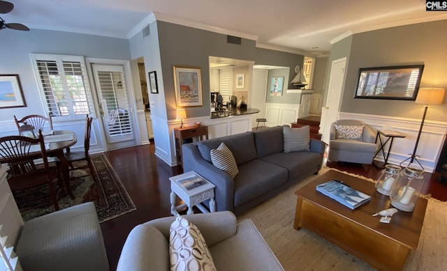 living room featuring visible vents, a wainscoted wall, ceiling fan, ornamental molding, and dark wood-style flooring