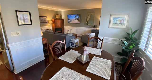 dining space featuring ornamental molding, wainscoting, a decorative wall, and wood finished floors