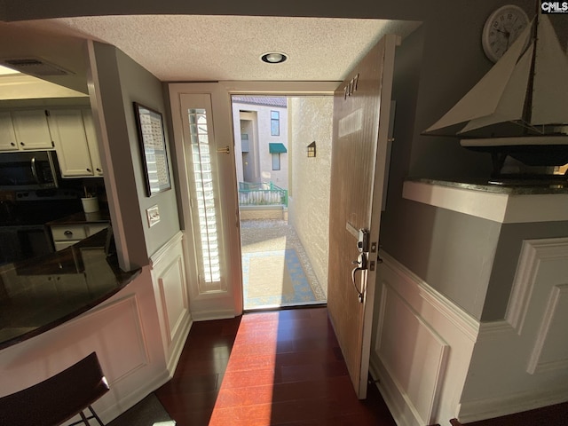 doorway to outside with a wainscoted wall, visible vents, a decorative wall, dark wood-type flooring, and a textured ceiling