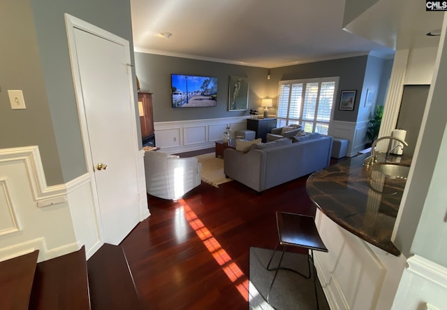 living room with dark wood-style floors, a decorative wall, a wainscoted wall, and crown molding