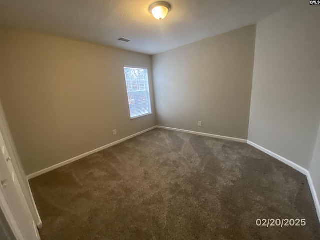 empty room featuring baseboards, visible vents, and dark carpet