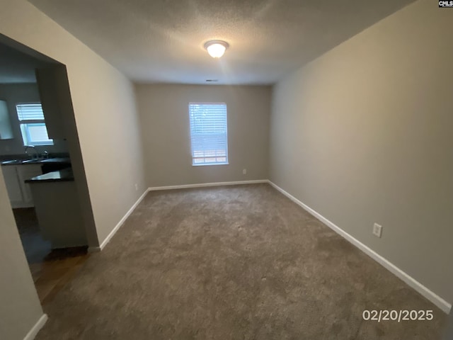 empty room with a textured ceiling, dark colored carpet, and baseboards