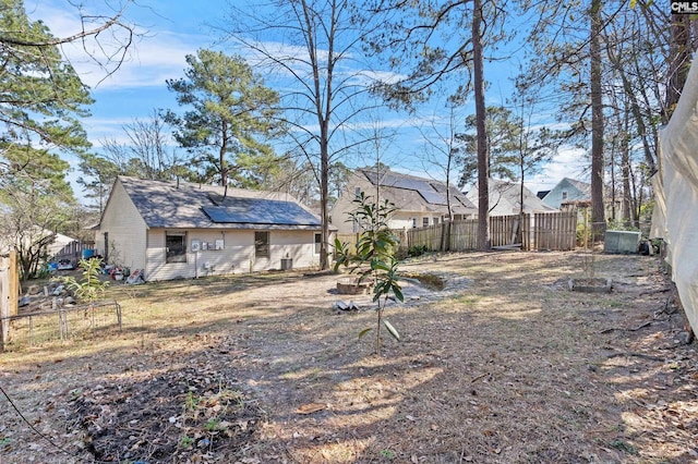 back of property with solar panels, roof with shingles, and a fenced backyard