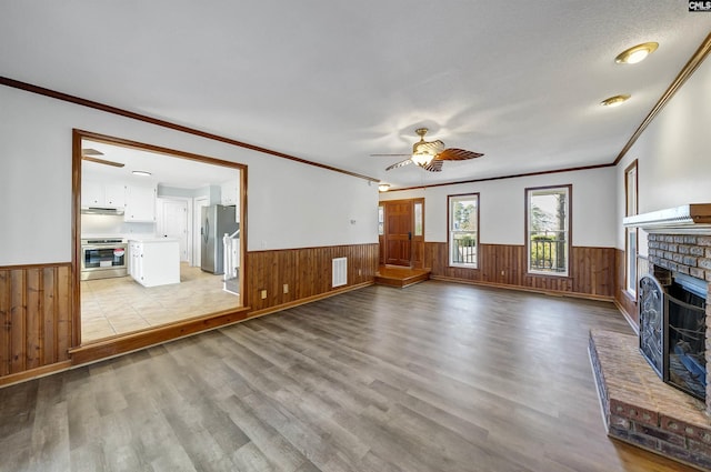 unfurnished living room featuring light wood-style floors, a fireplace, visible vents, and wainscoting