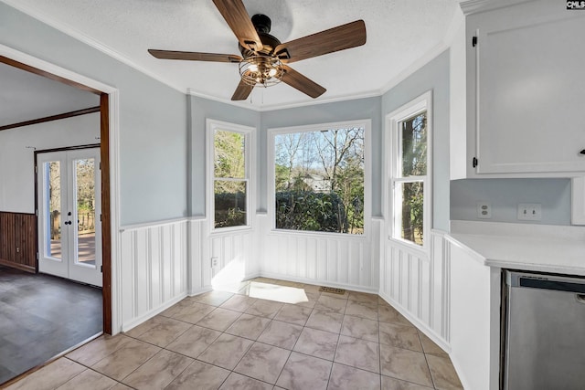 unfurnished dining area with a textured ceiling, ornamental molding, wainscoting, and a healthy amount of sunlight