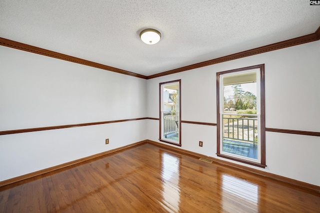 spare room with wood-type flooring, a textured ceiling, visible vents, and crown molding