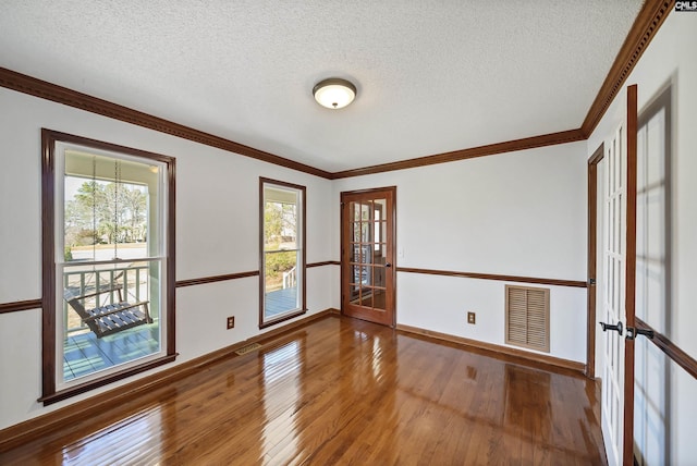 unfurnished room with a textured ceiling, wood-type flooring, visible vents, and crown molding