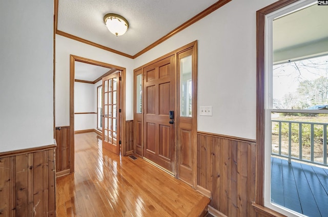 foyer with wainscoting, crown molding, a textured ceiling, and light wood finished floors