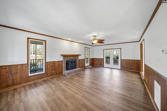 unfurnished living room with a brick fireplace, wood finished floors, french doors, and wainscoting